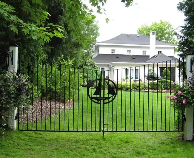 Black iron gate with circular emblem in front of a white house and green lawn