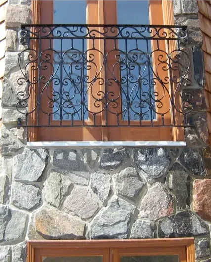 Stone facade with blue windows and an ornate black wrought-iron balcony