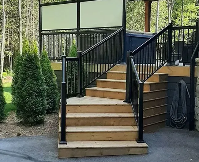 Wooden outdoor stairs with black railings leading to a deck in a wooded yard