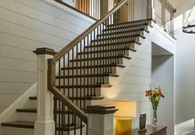 Interior staircase with dark wood railing, white walls, and a small table with a lamp and flowers