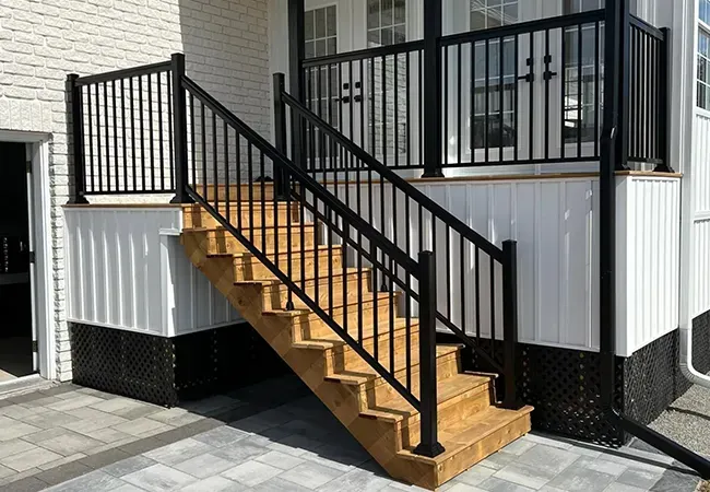 Wooden outdoor stairs with black railings leading to a raised porch beside a white house.