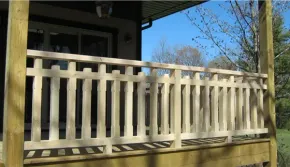 Light-colored wooden porch railing with alternating vertical slats against a dark house and blue sky.