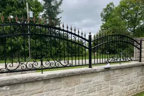 A decorative black wrought iron fence with arched tops and gold-tipped finials sits atop a light stone wall.