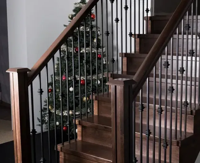 Indoor staircase with dark wood railing and black balusters beside a decorated Christmas tree