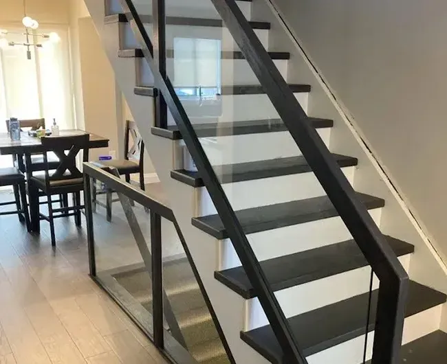 Modern indoor staircase with black railings beside a dining area and glass railing.