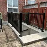 Concrete stairwell with black railings leading to a basement entrance beside a brick patio