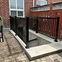 Concrete stairwell with black railings leading to a basement entrance beside a brick patio