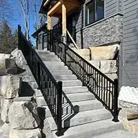 Stone steps with black railings leading up to a house entrance beside large rocks