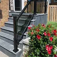 Front porch stairs with black railing beside a red flowering bush and brick house entrance
