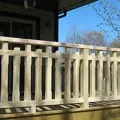 White wooden porch railing with vertical slats in front of a house, with blue sky behind