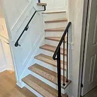 Wooden staircase with black handrails in a narrow indoor hallway