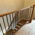Wooden staircase with black metal balusters and a light wood handrail along a hallway wall