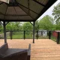 Covered wooden deck with black railing and a view of trees and a small shed in the yard.