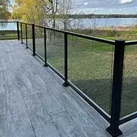 Glass railing on a gray wooden deck overlooking a grassy lakeside view