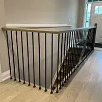 Black metal stair railing around an open stairwell in a bright hallway