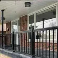 Covered porch with black railing, brick wall, and large windows on a house exterior.