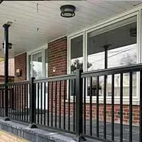 Covered porch with black railing, brick wall, and large windows on a house exterior.
