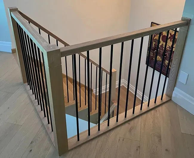 Wood staircase with black railings and light wood floors in a bright hallway