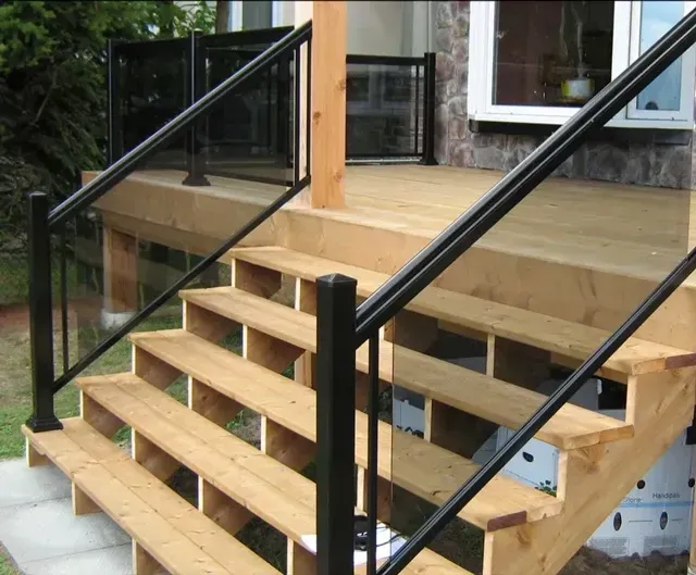 Wooden front porch stairs with black metal railings on a house exterior.