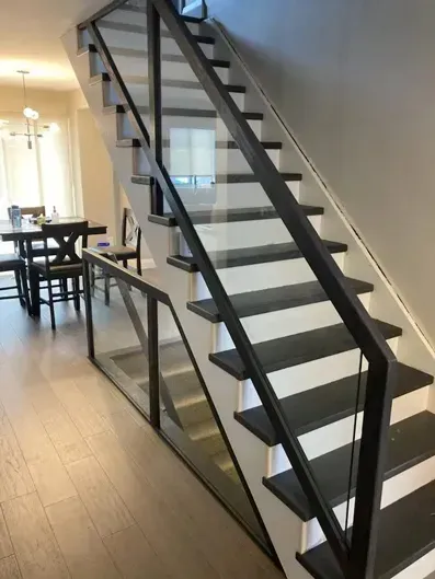 Modern indoor staircase with black railings and glass panels beside a dining area