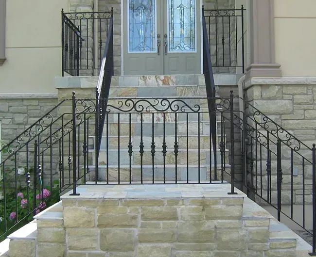 Front steps with black wrought-iron railings leading to a stone house entrance and double glass doors.