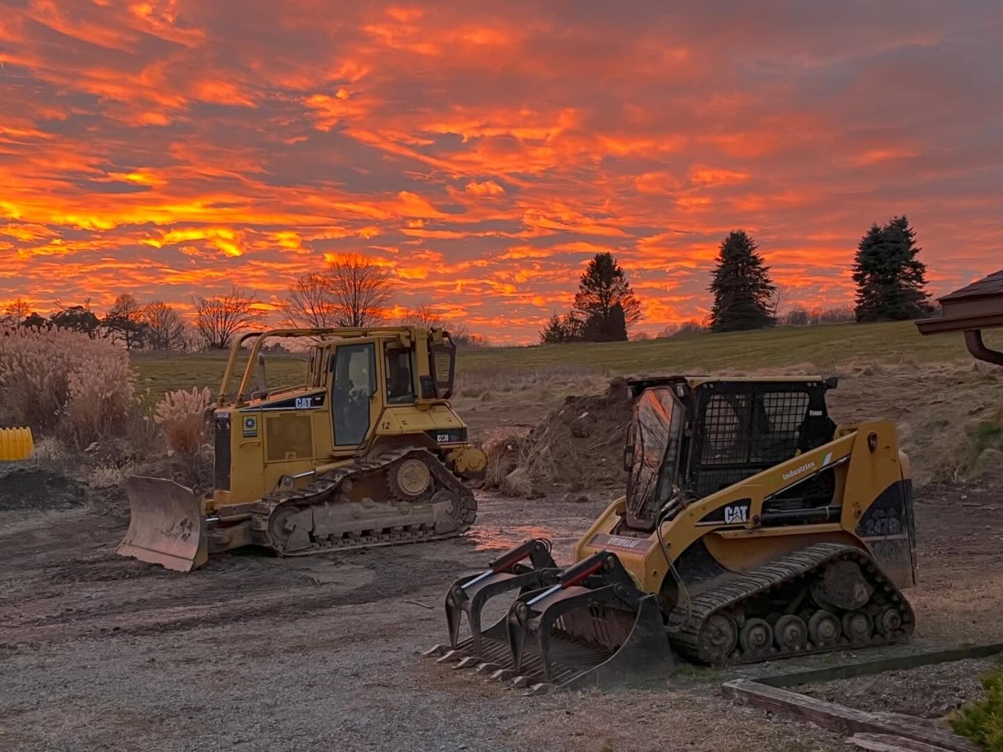 Two bulldozers are parked in a gravel lot at sunset.