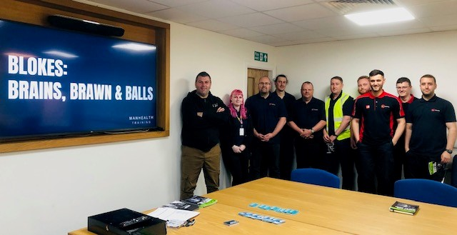 A group of men in a meeting room with a screen that says 