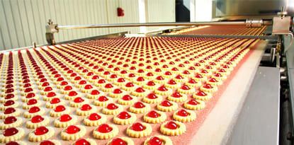 Rows of cookies with red centers moving along a conveyor belt in a factory.