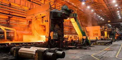 Inside a steel mill, machinery processes glowing hot metal.