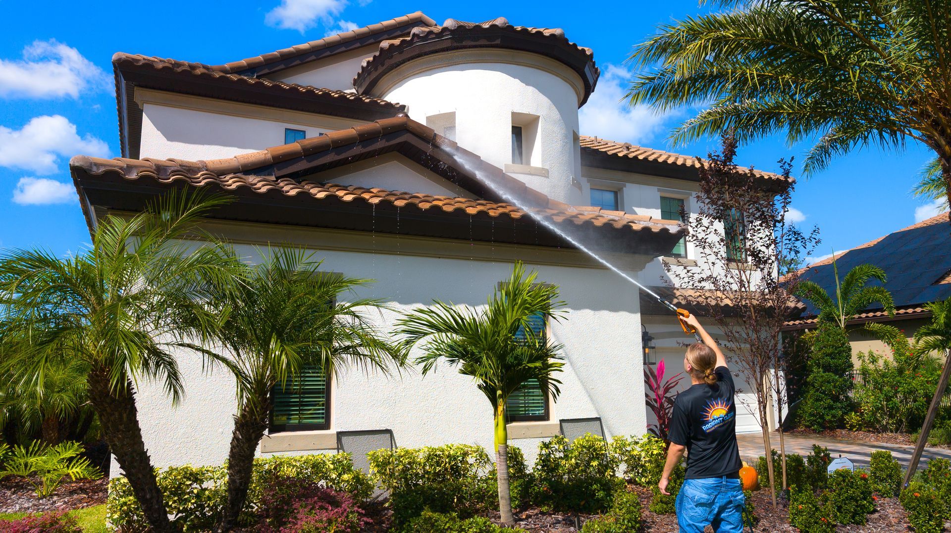 Spanish-style house with white stucco, terracotta roof, palm trees, and a person standing in the front yard