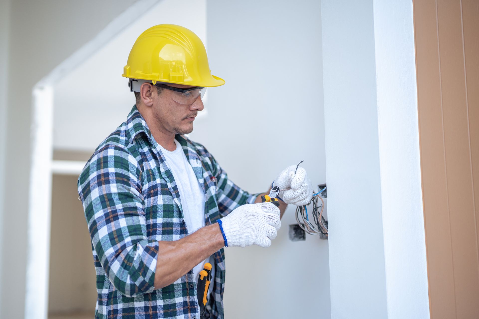A male electrician wearing gloves is installing wires at a newly constructed residential property.