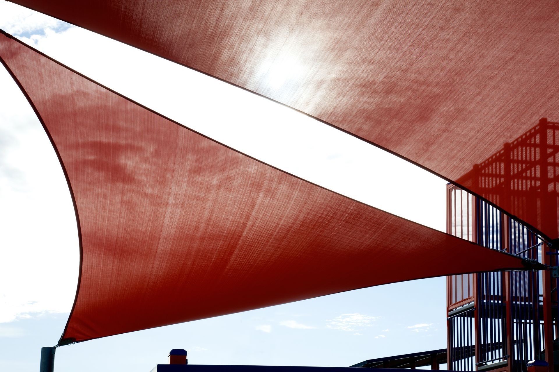 Red shade sail covering an intense sun glare above a kid's playground Red shade sail covering an intense sun glare above a kid's playground