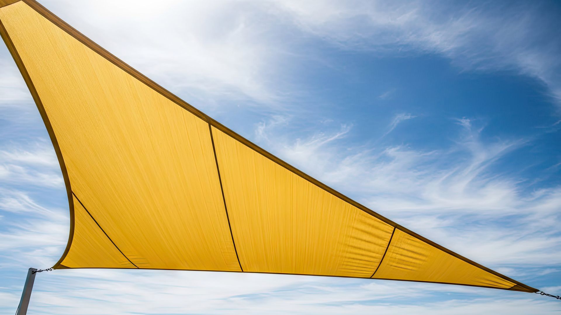 A vibrant yellow shade sail against a bright blue sky with wispy clouds.