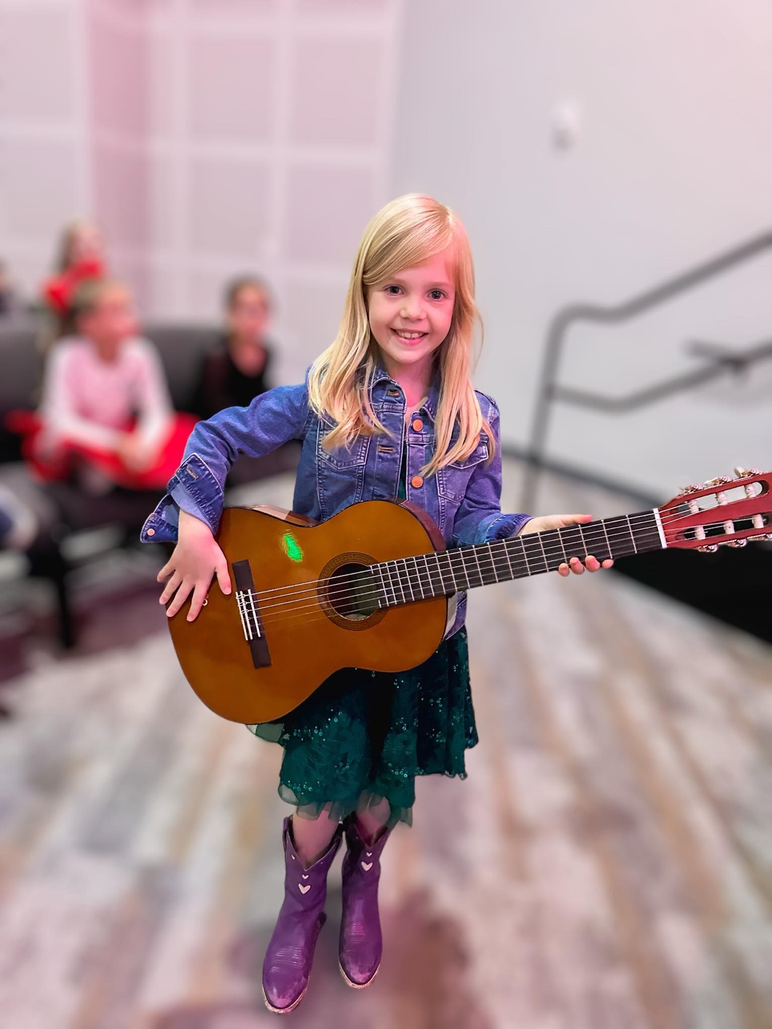 A little girl is holding a guitar in a room.