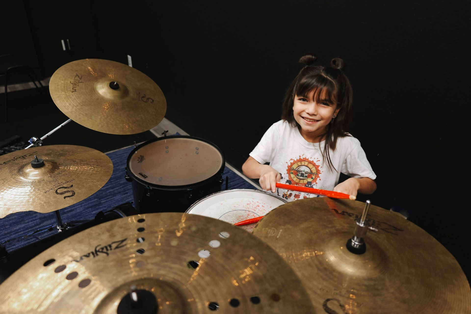 A little girl is playing drums in a dark room.