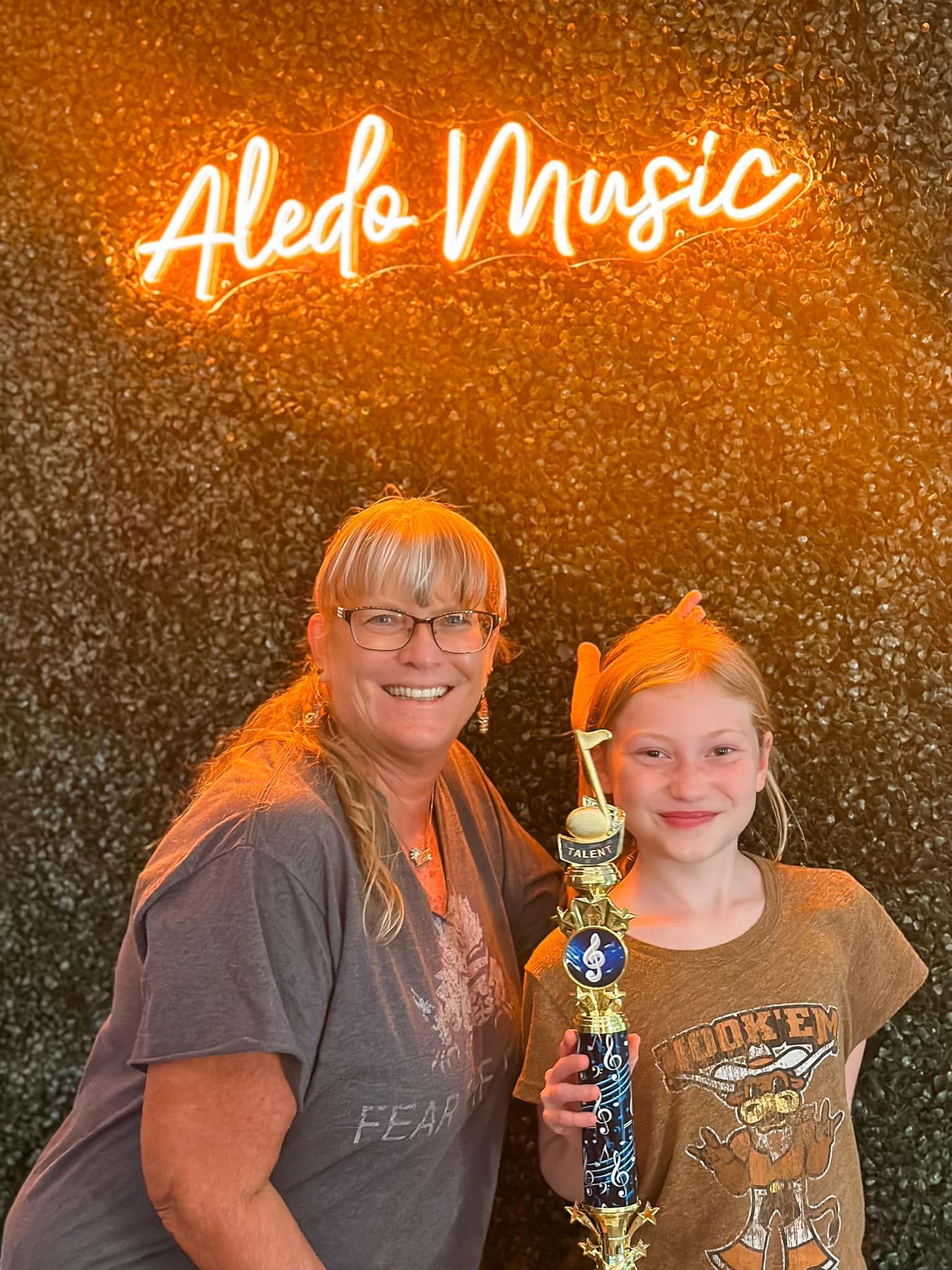 A woman and a girl are standing next to each other holding a trophy.