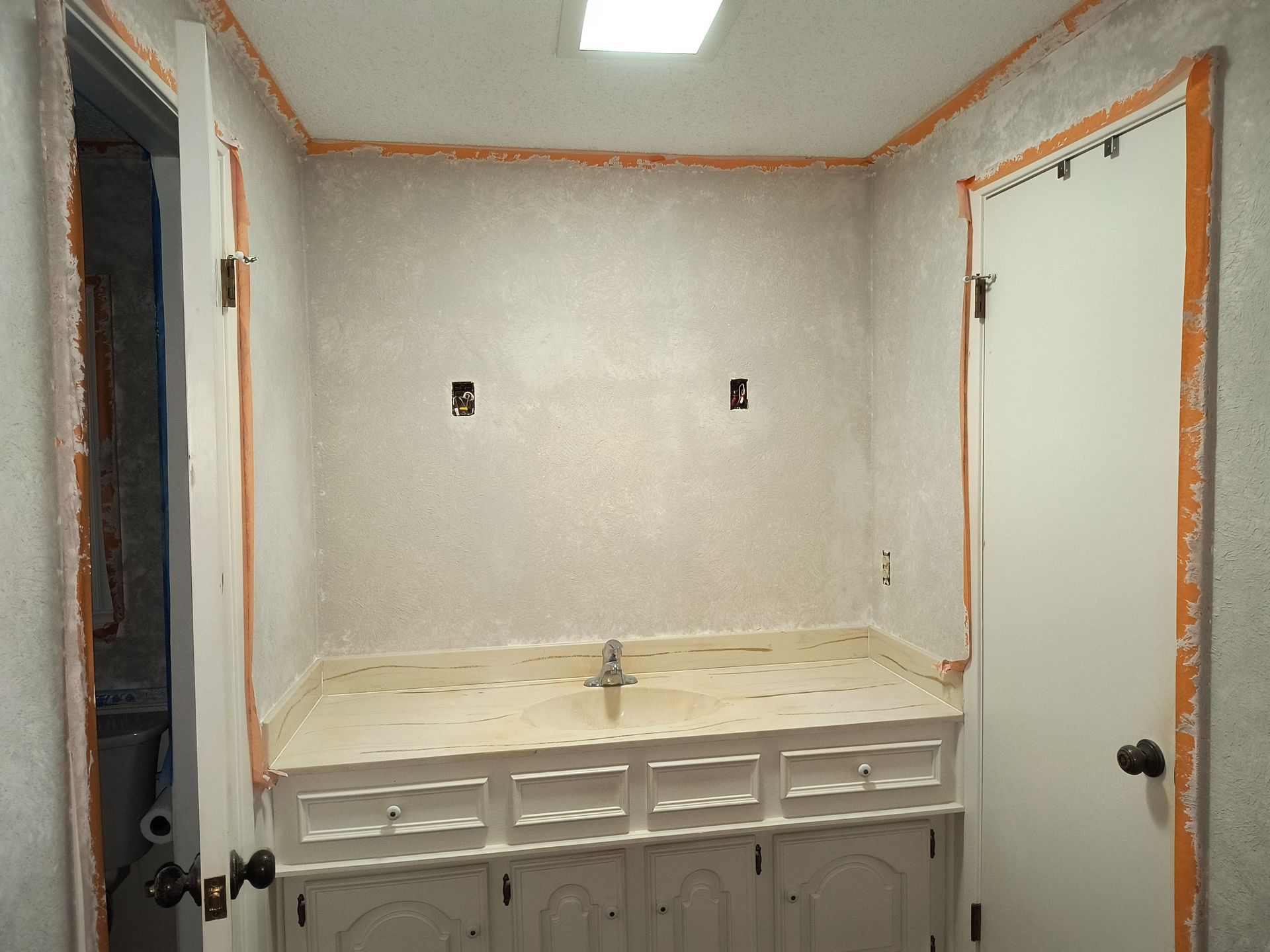 A bathroom vanity with a white cabinet, countertop sink, and unpainted walls with orange tape around the door frames.