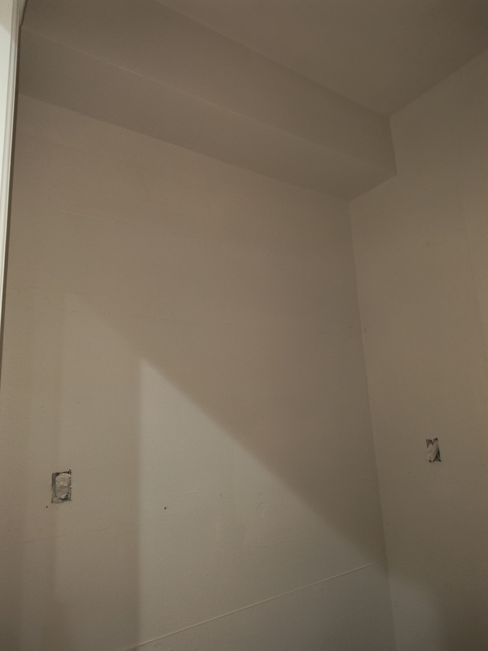 Interior corner of a beige-walled room with two electrical boxes and a recessed ceiling structure.
