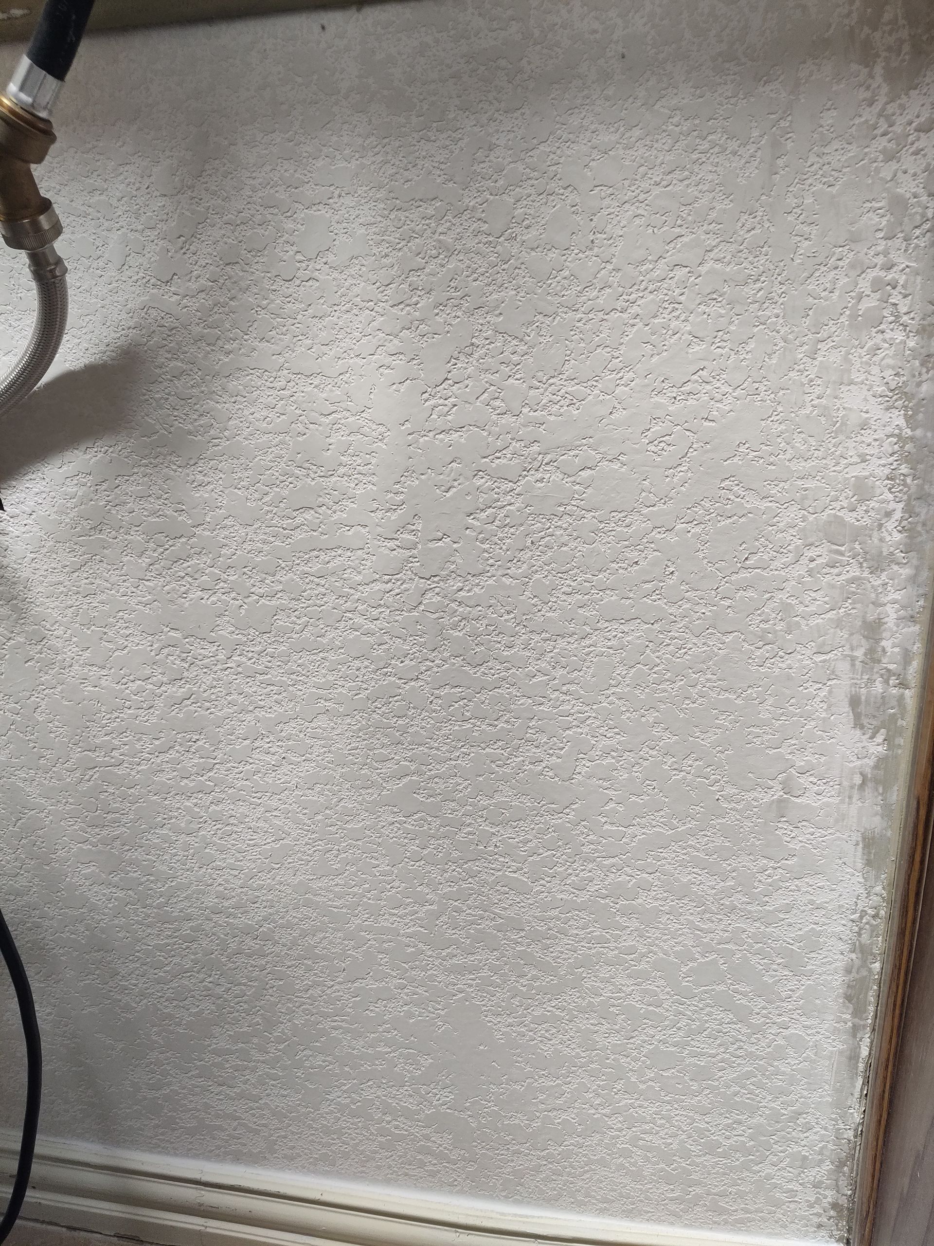 A close-up view of a textured, off-white wall with a metallic plumbing fixture visible in the upper left corner.