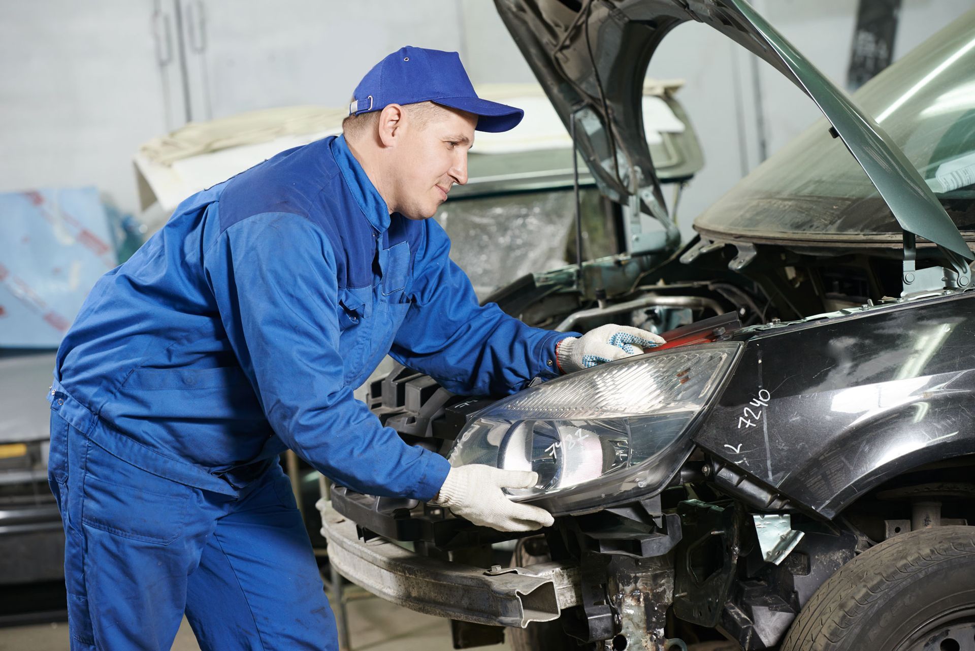 mechanic matching automobile headlight lamp to damaged car at repair service station