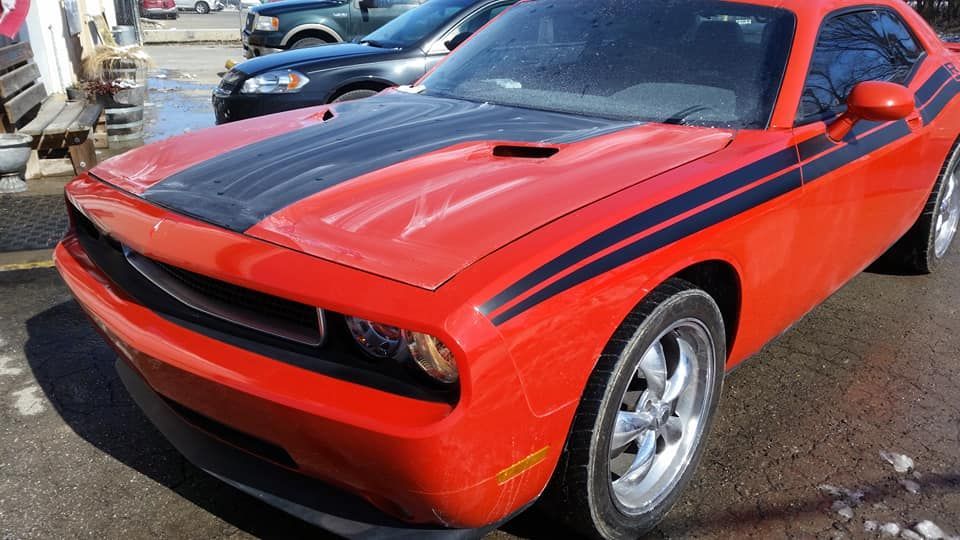 A red dodge challenger with black stripes on the hood is parked in a parking lot.