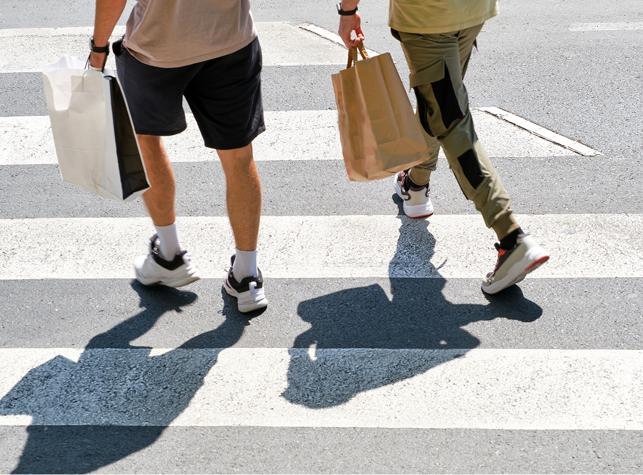 Two people are walking across a crosswalk carrying shopping bags.