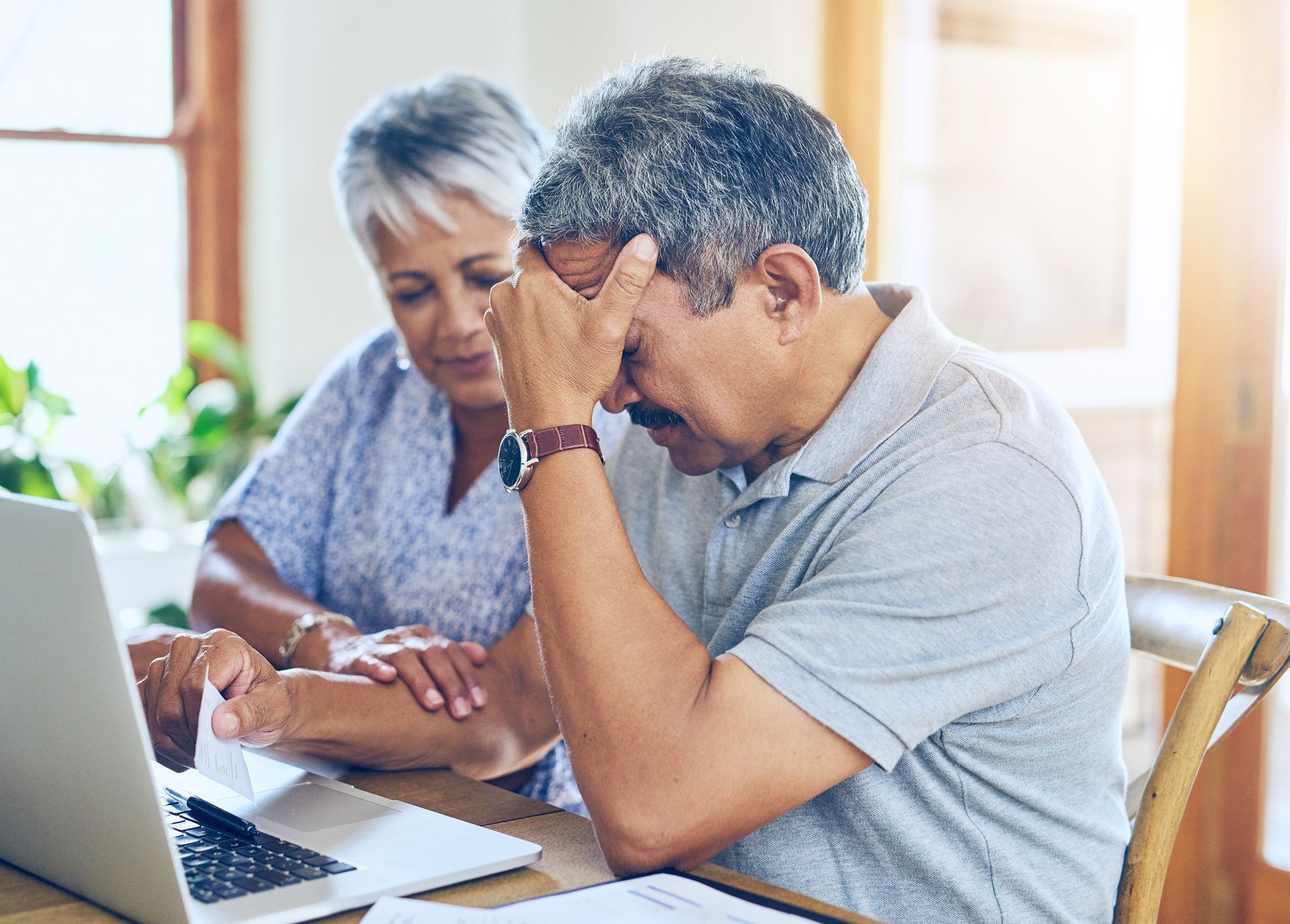 An elderly couple is sitting at a table looking at a laptop computer.