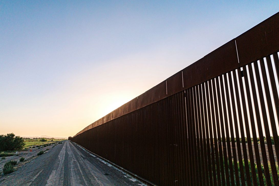 A fence along a dirt road with a sunset in the background.