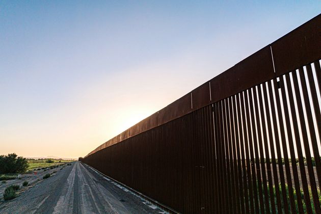 A fence along a dirt road with a sunset in the background.