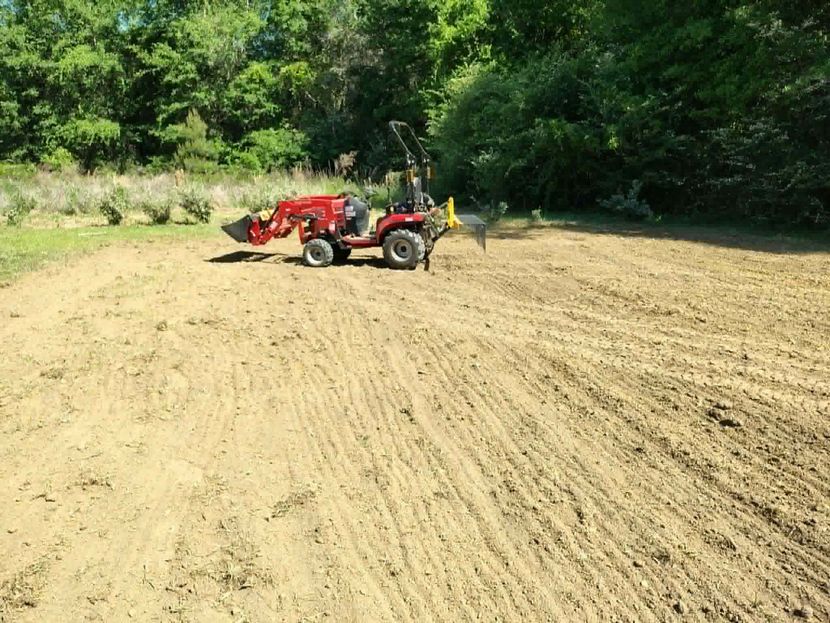 Red tractor grading a dirt field with trees in the background
