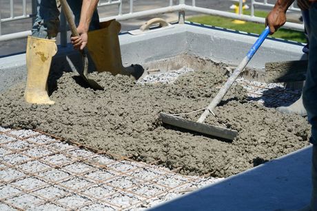 Workers leveling wet concrete with rakes and a screed at a construction site