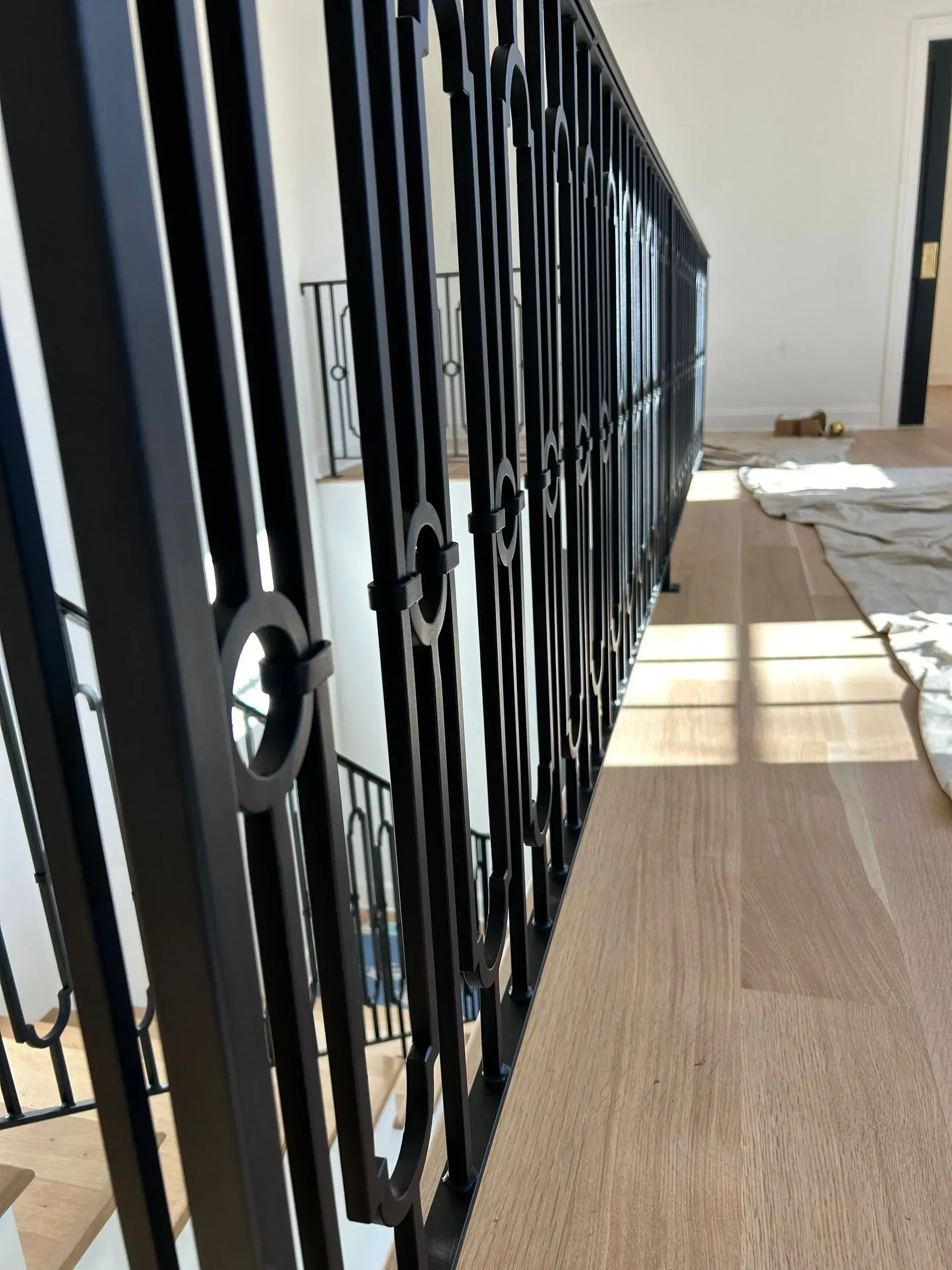 Black metal railing with decorative rings on light wood floor, leading to a stairwell.