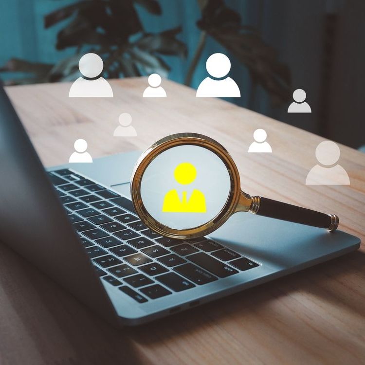 Magnifying glass on a laptop, highlighting a person icon. Other person icons float nearby, implying job searching.