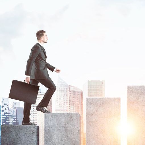 Businessman in suit climbs steps with briefcase, cityscape in background.